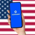 Logo de Coinbase en un smartphone frente a la bandera de Estados Unidos.